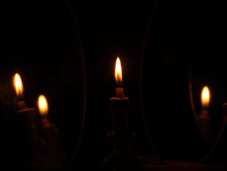 A candle burning in the dark is re-reflected in oval mirrors. Still-life.の写真素材