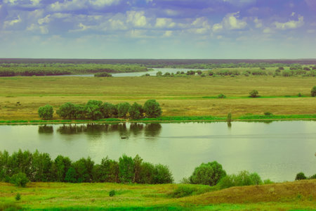 Sunny Russian summer landscape with a river in the fields and Cumulus clouds in the sky.
