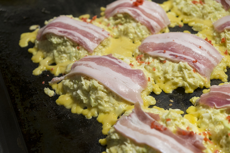 Okonomiyaki, Japanese pizza with bacon topping in cooking processの写真素材