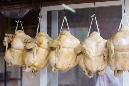Streamed chickens hanging behind glass cupboard in Hainanese chicken rice Thai restaurantの写真素材
