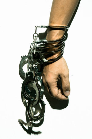 Harsh lighting image of hand being cuffed by many handcuffs, conceptual image of someone who keeps...
