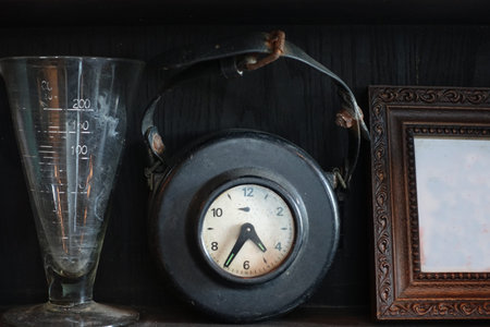 Old hang clock in black leather skin on shelf with other vintage decorations, old picture frame and...