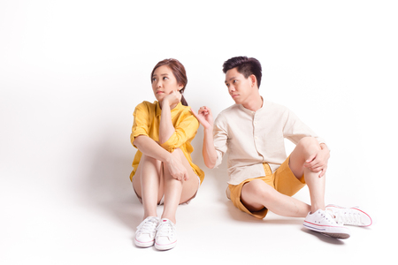 Young sulky asian female and young man trying to reconcile. sitting on white background