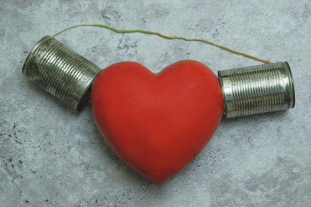 Red heart listening to tin can phone on gray background