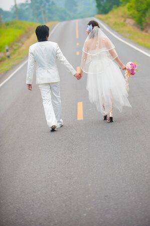 Wedding couple in wedding cloths walking along the roadの写真素材