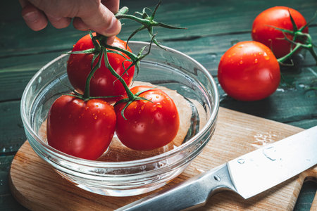 A branch of tomatoes in a bowl on a green wooden backgroundの写真素材