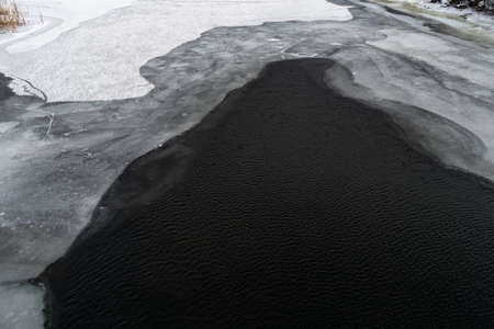dark water and white ice. cold ice. thawed patches. frozen river. landscape with a river in winter.の写真素材