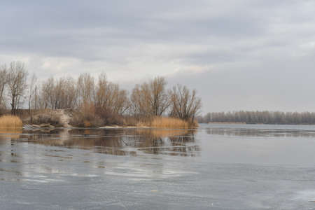 winter landscape with water. In front of a lake Panorama, mirror effect of the cloudy sky and the trees around it. Calm water and reflections from trees and sky. Pure Northern nature.の写真素材