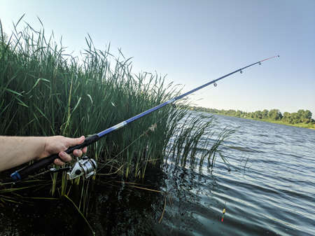 fishing on the river. fisherman with a fishing rod. catch . Fishing rod wheel closeup, man fishing with beautiful sunrise. little girl with a fishing rod and a bucket came fishing and looks at the pond.の写真素材