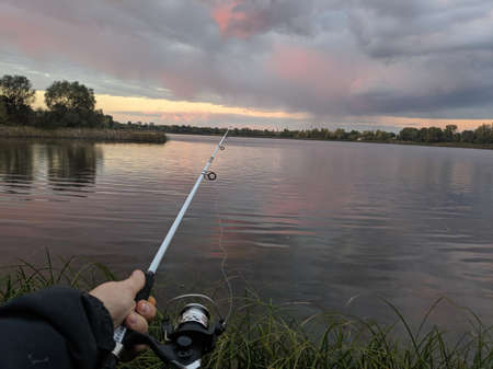 fishing on the river. fisherman with a fishing rod. catch . Fishing rod wheel closeup, man fishing with beautiful sunrise. little girl with a fishing rod and a bucket came fishing and looks at the pond.の写真素材