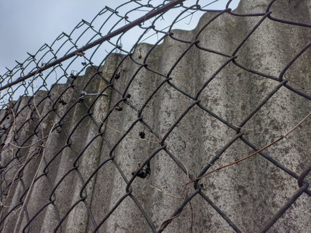fence made of metal and concrete. steel mesh. mesh fence. gray concrete fence. A metal door made of a steel grille covered in bronze is moving to the right, behind an old concrete wall.の写真素材