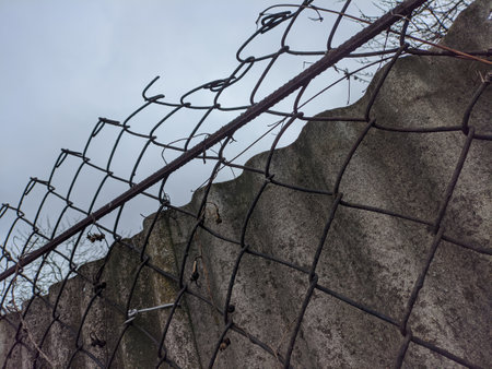 fence made of metal and concrete. steel mesh. mesh fence. gray concrete fence. A metal door made of a steel grille covered in bronze is moving to the right, behind an old concrete wall.の写真素材
