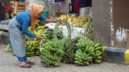 Magelang, Indonesia. March 11, 2021: An old woman selling fruit is cutting bananas at Muntilan Market, Magelangのeditorial素材