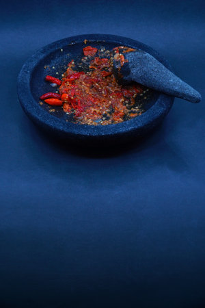 Red chili sauce on a stone mortar and pestle. Dark background, focus selected.の写真素材