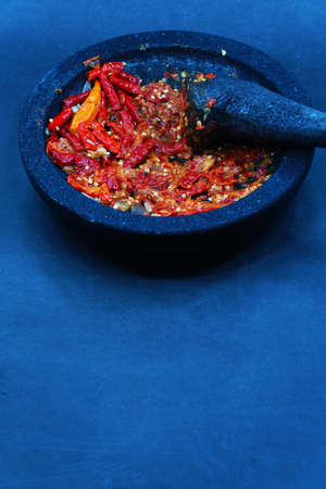 Red chili sauce on a stone mortar and pestle. Dark background, focus selected.の写真素材