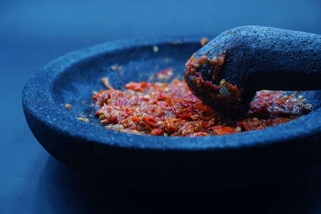 Red chili sauce on a stone mortar and pestle. Dark background, focus selected.の写真素材