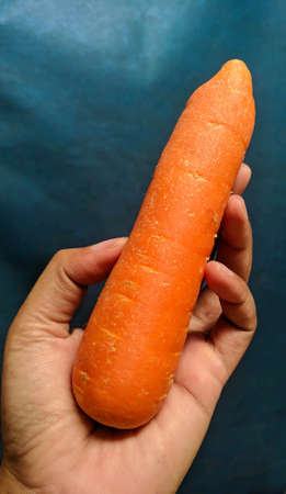 Carrot in man's hand on blue background. Focus selectedの写真素材