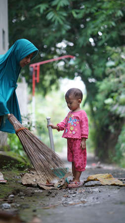 The little girl and her mother are sweeping the leaves in the yardの写真素材