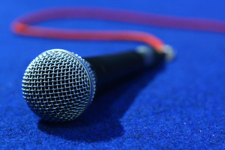 Microphone with red wire on blue carpet. Focus selected