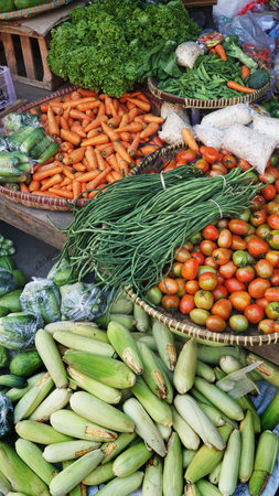 Various vegetables in bamboo baskets at the traditional market. There are tomatoes, long beans, carrots, corn. Focus selectedの写真素材
