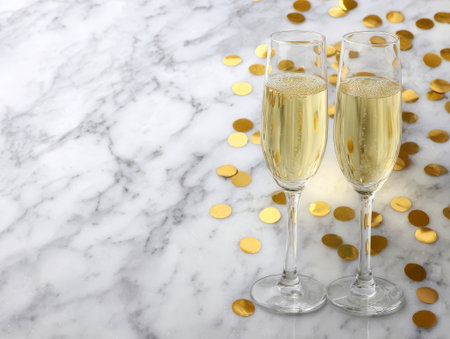 Two champagne glasses filled with golden drink on marble with confetti. Elegant holiday vibe creates a joyful atmosphere.の素材