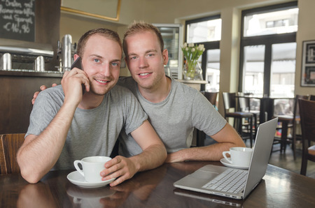 Shot of a young gays couple speaking on a phone with laptop  in a coffee shopの写真素材
