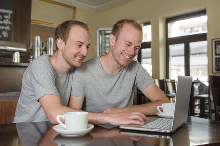gay couple looking at laptop with coffee in coffeehouseの写真素材