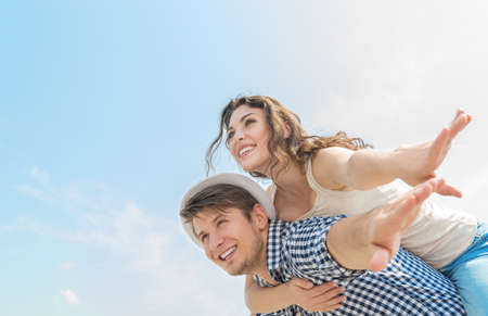 happy young man giving his girlfriend a piggyback ride outdoorsの写真素材