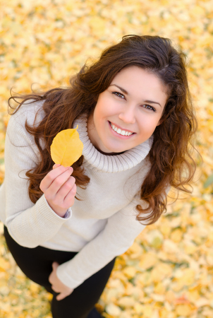 Closeup portrait of a beautiful and happy woman holding autumn leafの写真素材