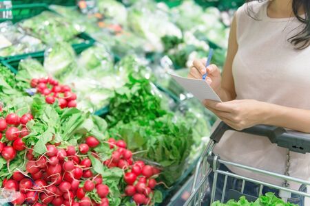 Close up shot  of young woman checking her grocery list while making a product choice in the supermarketの写真素材