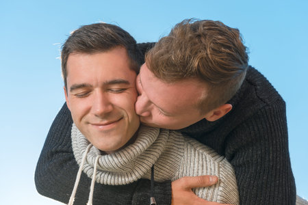  Gay couple,  hugs and kisses his boyfriend outdoors on a background of skyの写真素材