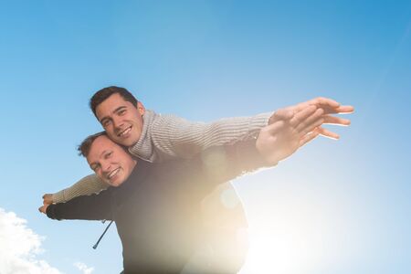 Homosexual couple fly with  his friend a piggyback ride on the sky backgroundの写真素材