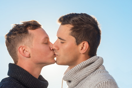 shot of a gay couple kissing each other on the background of the blue sky の写真素材