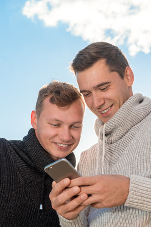 young gay couple using a mobile phone together at a outdoorの写真素材