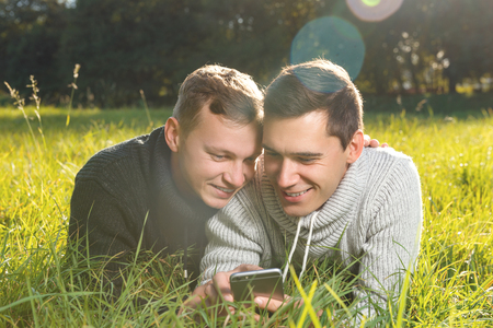  Horizontal shot  of a  young gays couple using smartphone  lying  on the grassの写真素材
