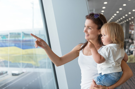 Young woman and her daughter looking out of the window while waiting on airport loungeの写真素材