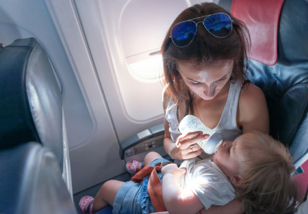 Young mother feeding her small daughter from bottle on airplaneの写真素材