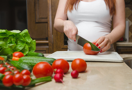 Pregnant woman cut fresh vegetables for salat close up の写真素材
