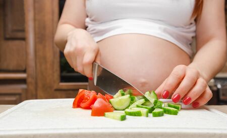Pregnant woman cut fresh vegetables for salat close upの写真素材
