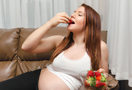 pregnant woman delicious eating strawberry in homeの写真素材
