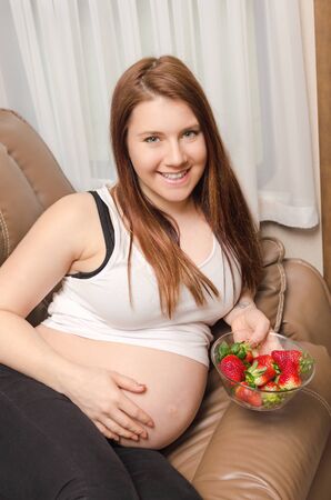 pregnant woman lying in the sofa and hold plate with strawsberryの写真素材