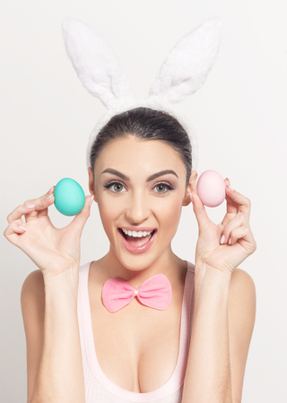 Studio shot of a smiling young woman wearing bunny ears and holding a of Easter eggs on light backgroundの写真素材
