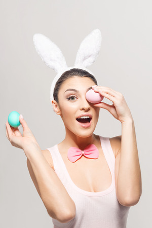Studio shot of a excited young woman wearing bunny ears and holding a of Easter eggs on light backgroundの写真素材