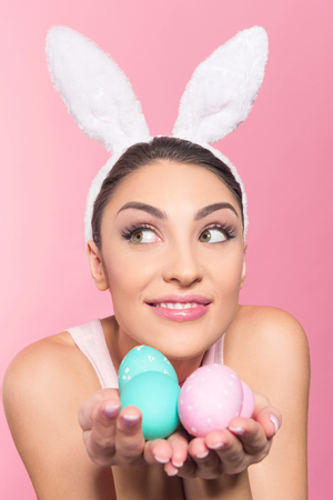 Happy young woman wearing bunny ears holding a handful of Easter eggs while watching on copy space textの写真素材