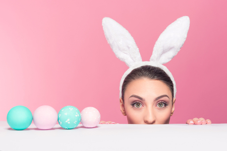 Studio shot of a young woman wearing bunny ears and peeking over a surfaceの写真素材