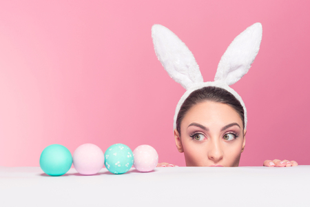 Studio shot of a young woman wearing bunny ears and peeking over a surface の写真素材