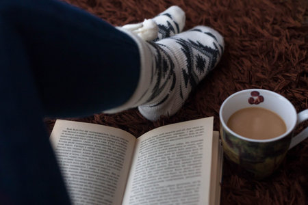 Female feet with a book and coffee on the wool rugの写真素材