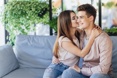 Young beautiful girl kisses handsome boy on summer terrace cafeの写真素材