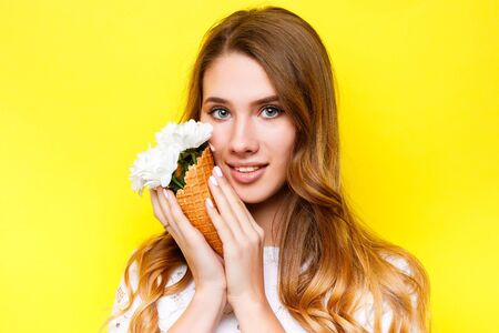 portrait of cheerful girl holding chrysanthemum flowers in the ice cream cone and looking at the camera on yellow background.の写真素材