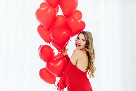 beautiful woman with heart shaped balloons standing ath the window and looking at the camera.の写真素材